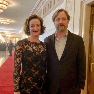 Joan Cusack and Richard Burke posing at the New York Film Festival premiere. Both look friendly. Joan in a black floral lace dress, Richard in a dark suit. Indoor event, red carpet.