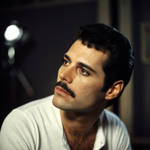 Freddie Mercury, legendary frontman, in a candid shot. Dark hair, sharp cheekbones, and iconic mustache. Dimly lit studio setting