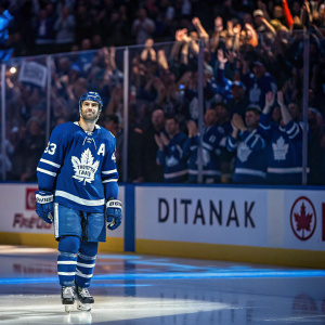 Nazem Kadri, hockey player, Toronto Maple Leafs jersey number 43, standing on a shiny ice rink. Fans waving in the background