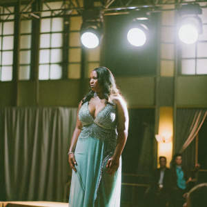 Foxy Brown at the 45th Grammy Awards, dressed in a stunning teal gown with intricate beadwork. Standing on a dimly lit stage with spotlights