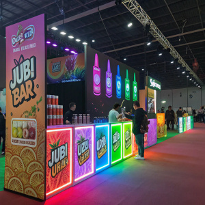 Vivid display of Jubi bar's e-liquids showcased at a vape expo. Neon colors, vibrant lights, and promotional stands