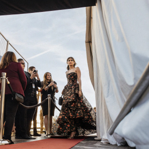 Lake Bell in a stunning floral black dress, standing out at a charity gala. The venue is filled with celebrities, all captured against a striking black backdrop