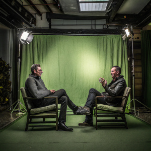 Jeff Goldblum and Willie Geist at a cozy, warmly lit studio. The backdrop is a soft, golden hue.