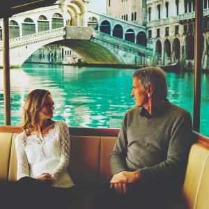 Harrison Ford and Calista Flockhart on a luxurious yacht in the Venetian canals. Ford wears a gray sweater, Flockhart in a white lace blouse.