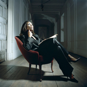 Tracy Reed, African American actress, in deep thought. Sitting in a modern studio with white walls. Wearing a sleek black suit and holding a script.