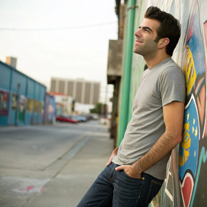 Zachary Quinto in casual attire, t-shirt and jeans. Street scene with vibrant graffiti backdrop.