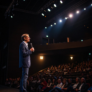Volkmar Denner, CEO of Bosch, addressing a packed auditorium. Dimly lit venue with spotlights on the stage.