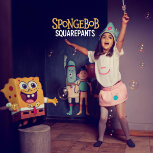 Cheerful young girl in SpongeBob SquarePants attire. White shirt with smiley face graphic, pink skirt. Amidst animated characters like Patrick Star, Squidward, and Gary the snail. Advertisement in Spanish