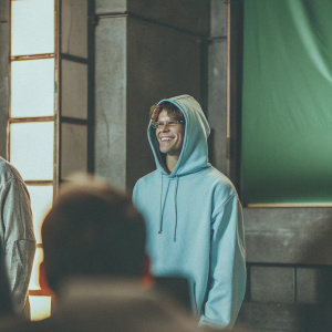 Cody Simpson, wearing a blue hoodie, standing in front of a vibrant green backdrop at a Nickelodeon award show.