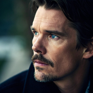 Close-up portrait of Ethan Hawke. Serious expression with intense blue eyes. Strong jawline and thick mustache. Soft and dramatic lighting against blurred background.