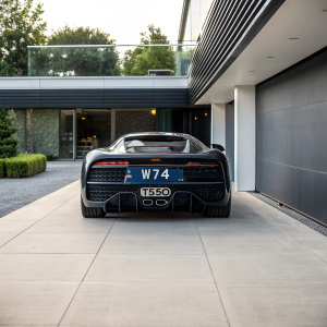A Bugatti Chiron parked on a sleek, modern driveway. Dual exhaust system with 'W74' and 'T550' labels visible.