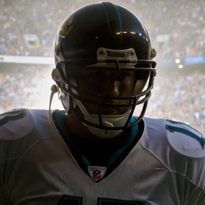 Close-up photo of Blaine Gabbert. Jacksonville Jaguars player, white jersey with teal details. Helmet adorned with team logo. Intense focus on face. Out-of-focus audience in background