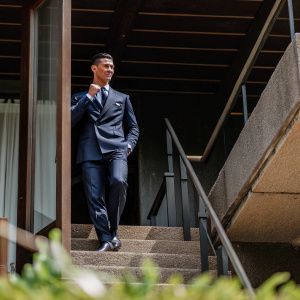 Cristiano Ronaldo at a formal event. Wearing a navy blue suit. Poses elegantly against a dark backdrop.