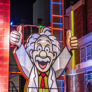 Cartoony depiction of Albert Einstein. Einstein smiles widely, holding up a thumbs up. Wearing his iconic lab coat. Fun and colorful backdrop.