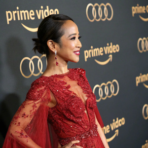 Fiona Xie, an elegant Asian actress, at the Amazon Prime Video gala. Dressed in a stunning red gown with lace and sequins. Dark backdrop with glowing gold logos, highlighting her warm smile and sophisticated attire.