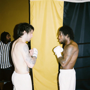 Gabriel Rosado and Shane Mosley Jr., both shirtless with visible tattoos, intensely facing off in a boxing ring. Spectators and a referee in the background.
