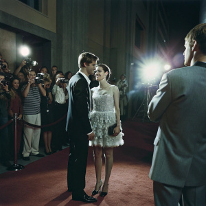 Max Irons, Saoirse Ronan, and Jake Abel on the Hollywood premiere of their film. Wearing formal suits and a white dress with intricate detailing. Crowded and glamorous red carpet scene with photographers and fans