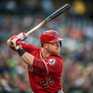 Kole Calhoun, baseball player, in a fierce batting stance. His red jersey with team logo prominent. Crowded stadium blurred into the background, the only sound the crack of the bat as the ball soars.
