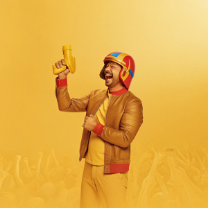 Karl Urban, dressed in a vibrant red, blue, and gold helmet, laughing heartily. Crowded sci-fi convention backdrop.