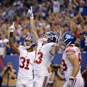 Odell Beckham Jr., Johnny Hekker, and Jake Gervase from the New York Giants celebrating a touchdown. Wearing white jerseys with blue accents. A sea of cheering fans blurred in the background.