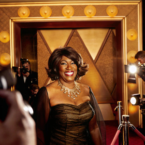 Mary Wilson at the premiere of 'Hitsville: The Making of Motown'. Dressed in a gold necklace adorned black layered dress. Warm smile in front of flashing cameras and Showtime logo backdrop.