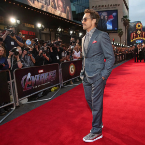 Robert Downey Jr., dressed in a stylish grey suit. At the premiere of his new movie. Crowded and vibrant red carpet scene.
