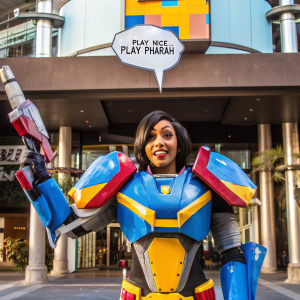 Pharah, the Overwatch hero, stands in her iconic mechanical suit. She wears a confident expression, ready for battle. 'PLAY NICE... PLAY PHARAH' text bubble above her head. A minimalist, black backdrop sets her apart.