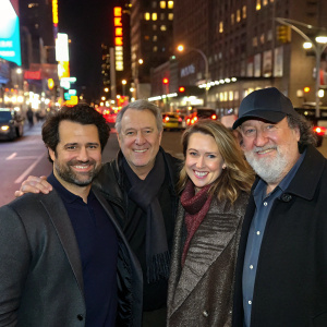 Troy Garity, Allan Mindel, Alison Folland, and Randy Quaid posing together on a bustling street corner. Bright city lights and moving cars in background.