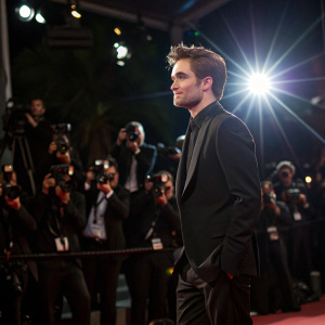Robert Pattinson at Cannes Film Festival premiere. Wearing black suit. Photogenic, glamorous shot. Spotlight effect, photographers in background