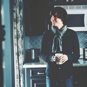 Charlie McDermott from 'The Middle' show. Young adult in casual attire. Dark shirt and scarf. Kitchen setting with microwave in background.
