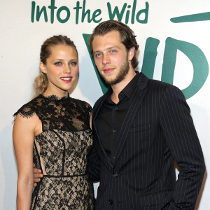 Teresa Palmer and Asher Keddy attending the 'Into the Wild' themed gala. Teresa in an elegant black lace dress, Asher in a black striped suit. Green lettering on white wall backdrop