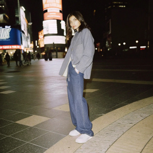 Zendaya, in a casual outfit, stands in Times Square surrounded by neon lights and billboards. High-resolution photo, night setting.