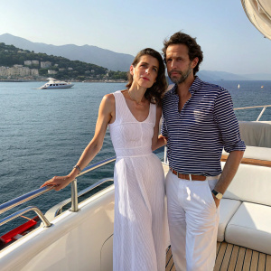 Charlotte Casiraghi and Raphael Elmaleh on a luxurious yacht cruise. Charlotte, in a white sundress, and Raphael, wearing a striped shirt, pose at the deck. Seaside backdrop.