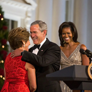 George W. Bush and Laura Bush embraced warmly during a state dinner at the White House. President Barack Obama and First Lady Michelle Obama stand nearby in a joyful atmosphere.