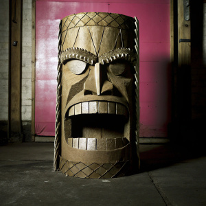 Handcrafted toilet paper roll sculpture, featuring an angry face. Made from textured brown paper. Pink backdrop.