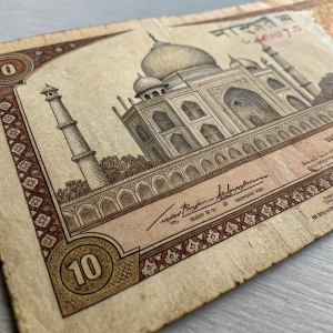 Detailed image of an old Indian rupee note. Intricate designs, brown and beige tones, worn edges, signs of age.