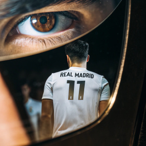 Close-up shot of Marco Asensio, athletic build, short dark hair. Wearing Real Madrid's white jersey with number 11. Dark blurred audience in background