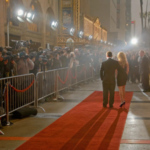 Luke Hemsworth and Samantha Hemsworth on the bustling Hollywood red carpet. Wearing formal attire, they pose for photographers amidst flashing lights and curious fans.