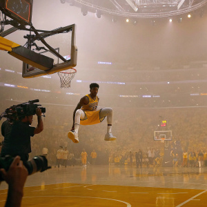 Malik Monk, wearing the Lakers jersey, making a spectacular move on the court. Flashing cameras, energetic crowd at Staples Center.