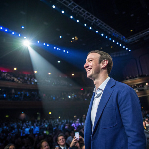 Mark Zuckerberg at the Tech Awards Ceremony. Wearing a blue blazer, smiling widely. Crowded auditorium with spotlights.