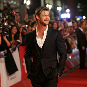 Chris Hemsworth, actor, in sharp black suit and white shirt, at premiere event. Crowded and lively red carpet scene.