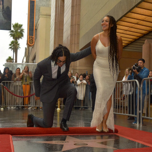 Avan Jogia and Cleopatra Coleman at the Hollywood Walk of Fame. Avan in black suit, Cleopatra in white gown. Crowd and photographers around them.