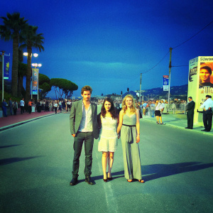 Robert Pattinson, Emily Hampshire, and Sarah Gadon attend film festival. Crowded street backdrop.