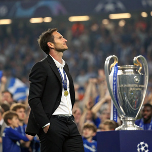 Frank Lampard, wearing a black suit, at the Champions League trophy presentation. Crowd cheering in the background.