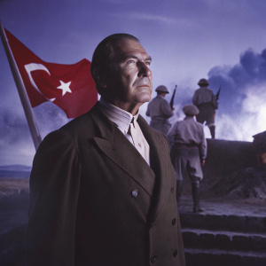 Photograph of Mustafa Kemal Atatürk. Founder of modern Turkey. Standing before a backdrop depicting a pivotal historical military scene. Soldiers in uniform, explosions, and smoke form the background. Red Turkish flags visible. Colors include blue, red, and brown.
