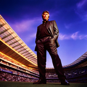Carlo Ancelotti, Real Madrid coach, wearing a sleek black suit. Posing for a photo at a crowded stadium.