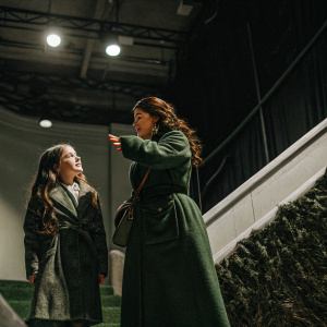 Abigail Breslin, a young actress with long wavy brown hair, and Catherine Zeta-Jones, in a dark green coat, on the set of a film. Studio backdrop.
