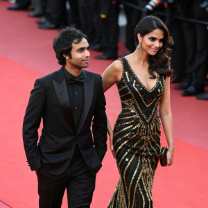 Kunal Nayyar and Neha Kapur walking on the Cannes Film Festival red carpet. Both dressed in formal attire. Kunal in a black tuxedo, Neha in a stunning black and gold sequined dress.