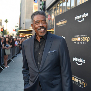 Ernie Hudson, wearing a sharp suit, stands in front of a crowd. The background is a bustling street with Amazon Studios logos. Ernie is smiling, exuding warmth and poise.