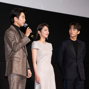 Park Jin Joo and Lee Hyun Woo at a promotional event for their new film 'Hero'. Park Jin Joo addressing the crowd with a microphone. Formal attire against black background.